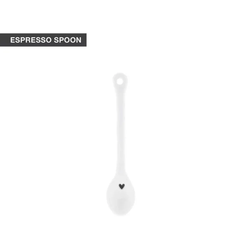 Ein weißer Espressolöffel aus Keramik mit einem kleinen schwarzen Herzdesign auf dem Griff, mit der Aufschrift „Bastion Collections – Löffel für Espresso wellenförmig“.