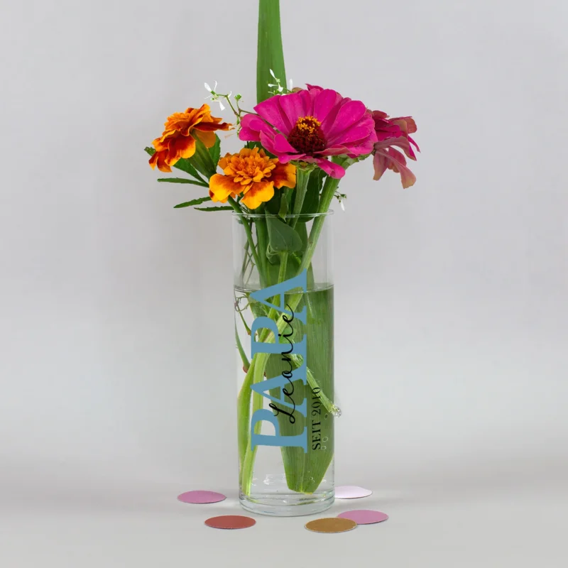 Kleine personalisierte Vase für Papa mit blauem Aufdruck, Wunschname und Jahreszahl, dekoriert mit farbenfrohem Blumenstrauß auf neutralem Hintergrund