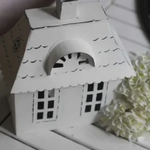 Ein VL Home – Metallhaus weiß mit Walmdach klein auf einem Holztisch.